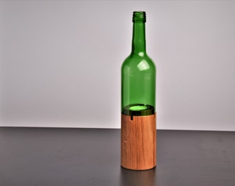 May include: A green glass wine bottle with a wooden base. The bottle is empty and has a clear glass top.