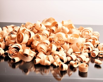 May include: A large pile of light brown wood shavings, curled into spirals, on a black surface.