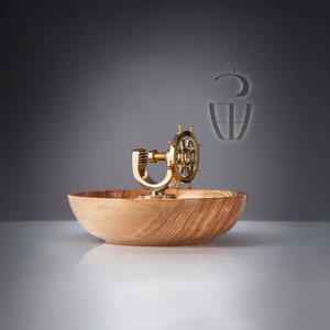 Peut inclure: Un bol en bois avec un gouvernail doré et un support en forme de U. Le bol présente un fini naturel veiné. Le gouvernail est monté sur le bord du bol. Le fond est un dégradé de gris.