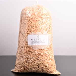 Puede incluir: Una gran bolsa de plástico transparente llena de virutas de madera de color marrón claro. Una etiqueta blanca con texto negro está adherida a la parte delantera de la bolsa. El texto de la etiqueta está en alemán.