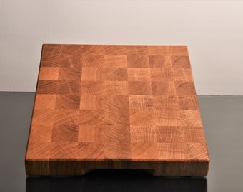May include: A large, square, wooden cutting board with a checkered pattern. The board is made of light brown wood and has a natural finish.