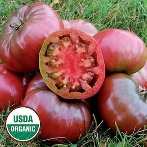 May include: A close-up of a group of dark red tomatoes with a green stem. One tomato is cut in half, revealing a red interior with black seeds. The tomatoes are labeled "USDA Organic".