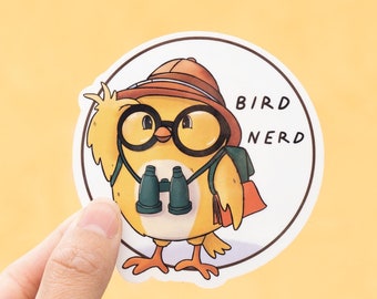 Könnte beinhalten: Ein gelber Vogel mit braunem Hut und Brille, der ein Fernglas hält. Der Vogel trägt einen Rucksack und hat den Text "BIRD NERD" auf dem Aufkleber.