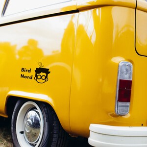 May include: A yellow vintage van with a black decal of a person wearing glasses with a bird on their head. The decal says "Bird Nerd".