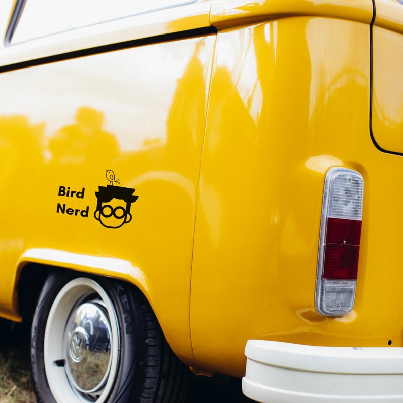 May include: A yellow vintage van with a black decal of a person wearing glasses with a bird on their head. The decal says "Bird Nerd".