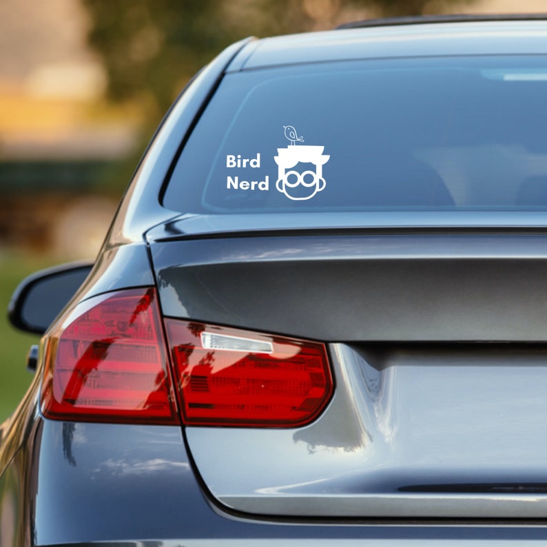 May include: A white vinyl sticker with a cartoon illustration of a person wearing glasses with a bird perched on their head. The text "Bird Nerd" is below the illustration.