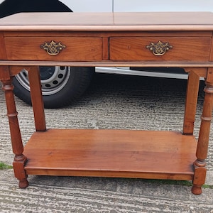 May include: A wooden console table with two drawers and a lower shelf. The table has a dark brown finish and features ornate brass drawer pulls.
