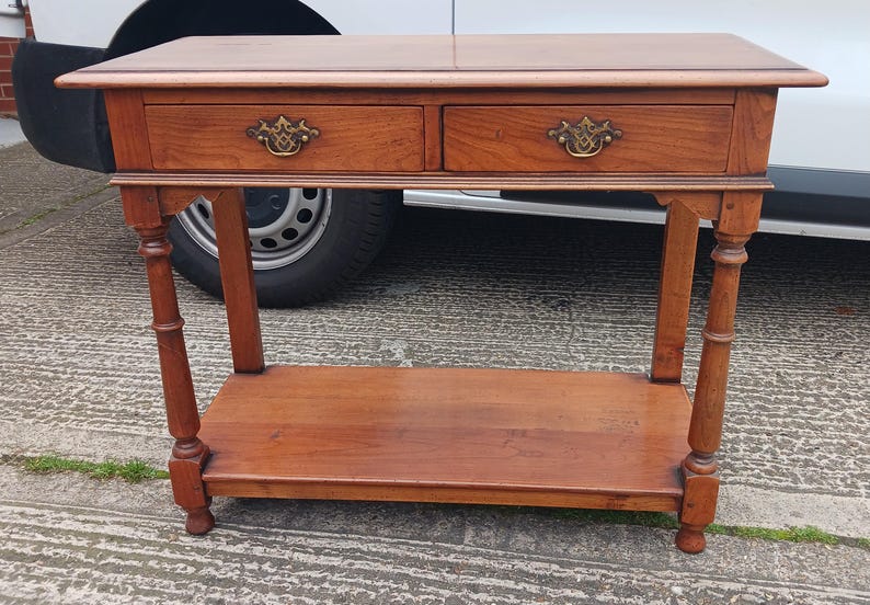 May include: A wooden console table with two drawers and a lower shelf. The table has a dark brown finish and features ornate brass drawer pulls.