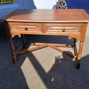 May include: A wooden side table with two drawers and a rectangular top. The table has a warm brown finish, with decorative details on the drawer fronts and legs. The table is approximately 76 cm long, 46 cm wide, and 71 cm high.