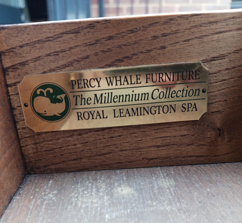 May include: A gold metal plaque with the text "Percy Whale Furniture The Millennium Collection Royal Leamington Spa" and a green whale logo.