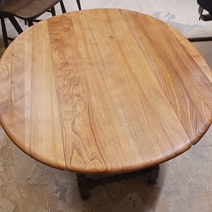 May include: A round wooden table with a light brown finish. The table has three leaves that can be extended to make it larger. The table is made of solid wood and has a natural grain pattern.
