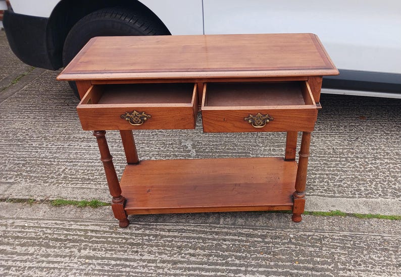 May include: A wooden side table with two drawers and a lower shelf. The table has a light brown finish and brass hardware.