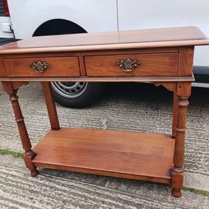 May include: A wooden console table with two drawers and a lower shelf. The table has a dark brown finish and features brass hardware.