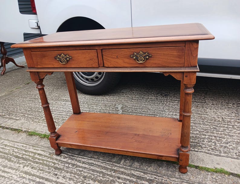 May include: A wooden console table with two drawers and a lower shelf. The table has a dark brown finish and features brass hardware.