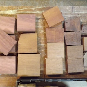 May include: A collection of various square and rectangular wooden blocks in different shades of brown, ranging from light tan to deep reddish-brown, arranged in a loose grid pattern with visible wood grain textures on their flat surfaces.
