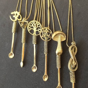 May include: Seven gold necklaces with different pendants, each with a small spoon at the end. The pendants include an Om symbol, a tree of life, a star of David, a mushroom, and a snake.