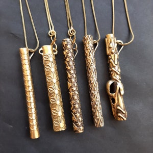 May include: Five gold necklaces with different patterned cylindrical pendants. The pendants are all about the same length and have various intricate designs.