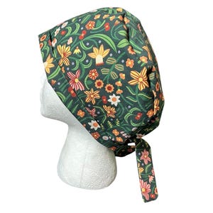 May include: A dark green scrub cap with a floral pattern featuring yellow, orange, and pink flowers, and green leaves. The cap is tied at the back with a matching fabric tie. The cap is on a white mannequin head.