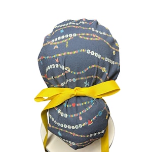 May include: A dark blue scrub cap with a repeating pattern of colorful strings of charms and the words "LOVE" and "MAKE". The cap is tied with a bright yellow ribbon.