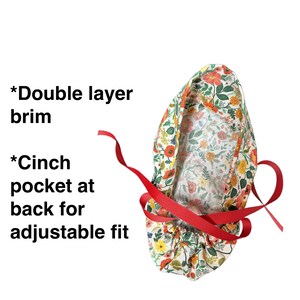 K&ouml;nnte beinhalten: OP-Haube mit floralem Muster, doppellagigem Rand und Kordelzugtasche f&uuml;r eine verstellbare Passform. Die Haube hat ein Muster aus roten, orangen und gelben Blumen auf wei&szlig;em Grund, gebunden mit einem roten Band.