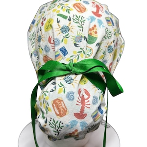 May include: A white scrub cap with a green ribbon bow. The cap is patterned with colorful illustrations of sardines, crabs, fish, and lemons. The cap is designed to be worn in a medical or culinary setting.
