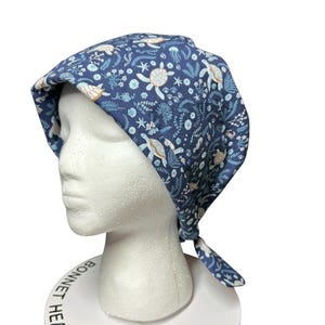 May include: A navy blue head covering featuring a sea turtle and floral design. The head covering is tied at the back and displayed on a white mannequin head. The text "BONNET HEAD DESIGNS" is printed on the base.