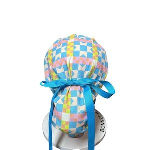 May include: A colorful scrub cap with a geometric pattern in pastel colors of blue, yellow, and pink. The cap is tied with a bright blue ribbon. The cap is designed to be worn in a medical or healthcare setting.