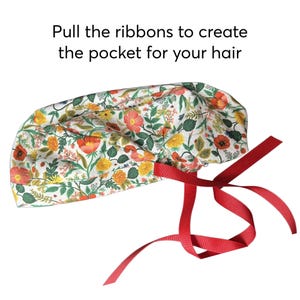 K&ouml;nnte beinhalten: Eine OP-Haube mit floralem Muster und roten B&auml;ndern. Die Haube hat einen wei&szlig;en Hintergrund mit orangefarbenen, gelben und gr&uuml;nen floralen Designs. Der Text "Ziehen Sie die B&auml;nder, um die Tasche f&uuml;r Ihr Haar zu erstellen" befindet sich &uuml;ber der Haube.