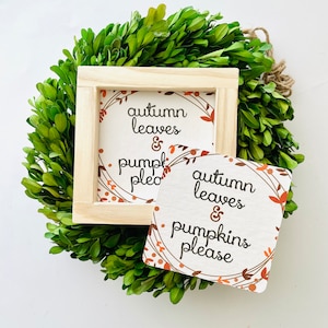 May include: Two signs with an autumn theme. The signs are made of wood and have a white background with brown floral designs. The text on the signs reads "autumn leaves & pumpkins please".