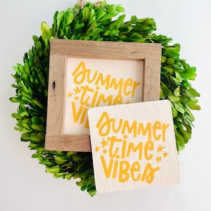 May include: A wooden framed sign with the text "Summer Time Vibes" in yellow lettering with stars on a white background. The sign is sitting on a green wreath.
