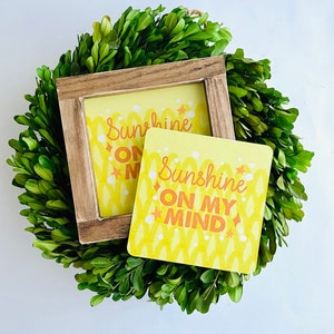 May include: Two yellow coasters with a white and orange pattern. The coasters feature the text "Sunshine on my mind".