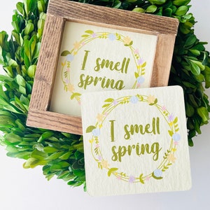 May include: Two wooden signs with a floral wreath design and the text "I smell spring" in green lettering.