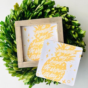 May include: Two white signs with a yellow pineapple graphic and the text "A pineapple a day keeps the worries away". The signs are on a green leafy background.