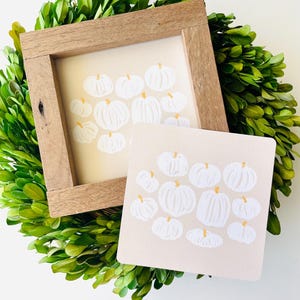 May include: Two framed illustrations of white pumpkins on a beige background. The pumpkins are arranged in a cluster and have a simple, hand-drawn style.