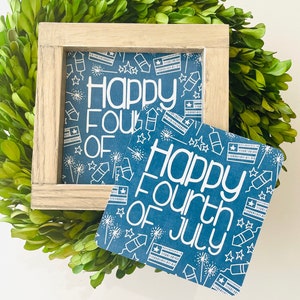 May include: Two blue and white signs with a white background and a blue pattern of stars, fireworks, and American flags. The signs read "Happy Fourth of July".