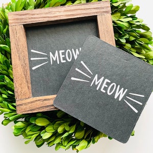 May include: Two black chalkboard signs with a wooden frame. The signs say "MEOW" in white text with white cat whiskers.