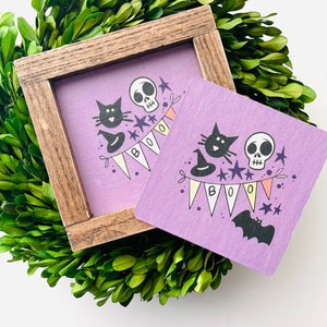May include: A purple wooden sign with a black cat, skull, and bat illustration. The sign says "BOO" with colorful pennants.