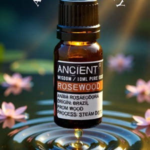 May include: A brown glass bottle of Rosewood essential oil with a black cap. The label reads "Ancient Wisdom" and "10ml Pure". A drop of oil falls into water, creating ripples. The text "A Drop of Clarity" is arched above the bottle.