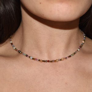 Puede incluir: Un delicado collar de cuentas con una variedad de pequeñas cuentas de colores. El collar está compuesto por un hilo de diminutas cuentas redondas en tonos rosa, verde, dorado y marrón. El collar se lleva alrededor del cuello.