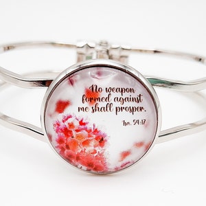 May include: Silver bangle bracelet with a round glass charm featuring a floral design and the text "No weapon formed against me shall prosper. Isa. 54:17"