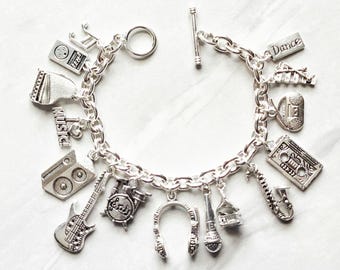 May include: A silver-tone charm bracelet featuring various music-themed pendants including a guitar, drum set, headphones, microphone, saxophone, cassette tape, boombox, piano, and a charm with the text "I love music" and "Dance".