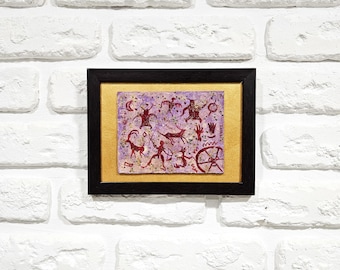 May include: A framed artwork depicting a purple and red cave painting with figures of animals and humans. The artwork is framed in a black frame with a gold mat.
