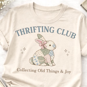 May include: A white ceramic mug with a black handle and the text "But First, Coffee" in a bold, black font. The mug is set against a blurred background, suggesting a cozy setting.