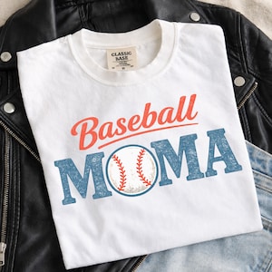 May include: White t-shirt with the words "Baseball MOMA" in red and blue, featuring a baseball graphic. The shirt has a classic fit and a tag that reads "CLASSIC BASE". The shirt is displayed on a black leather jacket and blue jeans.