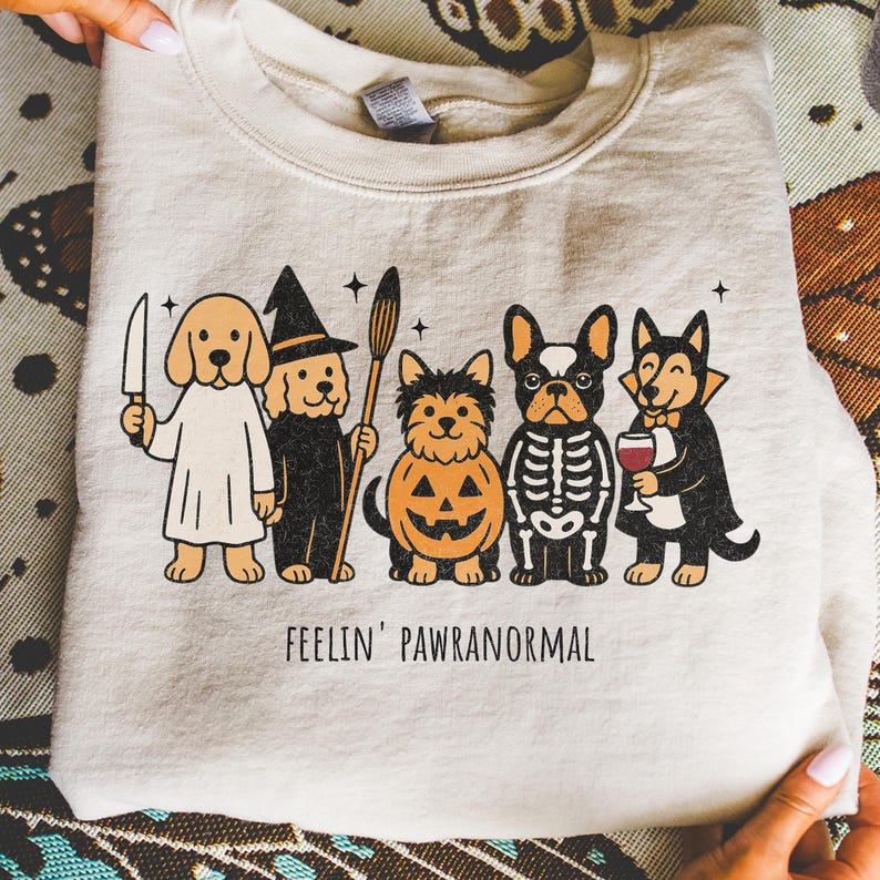 Halloween PNG for download - funny dogs in halloween costumes with quote feelin pawranormal. Halloween-themed graphic of five cartoon dogs dressed in costumes. The dogs are dressed as a ghost, witch, jack-o'-lantern, skeleton, and vampire. The text "FEELIN' PAWRANORMAL" is printed below the dogs.