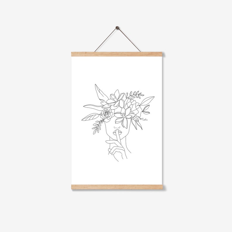 K&ouml;nnte beinhalten: Minimalistischer Kunstdruck mit einer Frau mit Blumenkranz, die einen Finger an den Lippen hat. Das Kunstwerk zeigt eine Geste der Stille. Das Bild ist auf wei&szlig;em Hintergrund und wird von einem Holzrahmen gehalten.