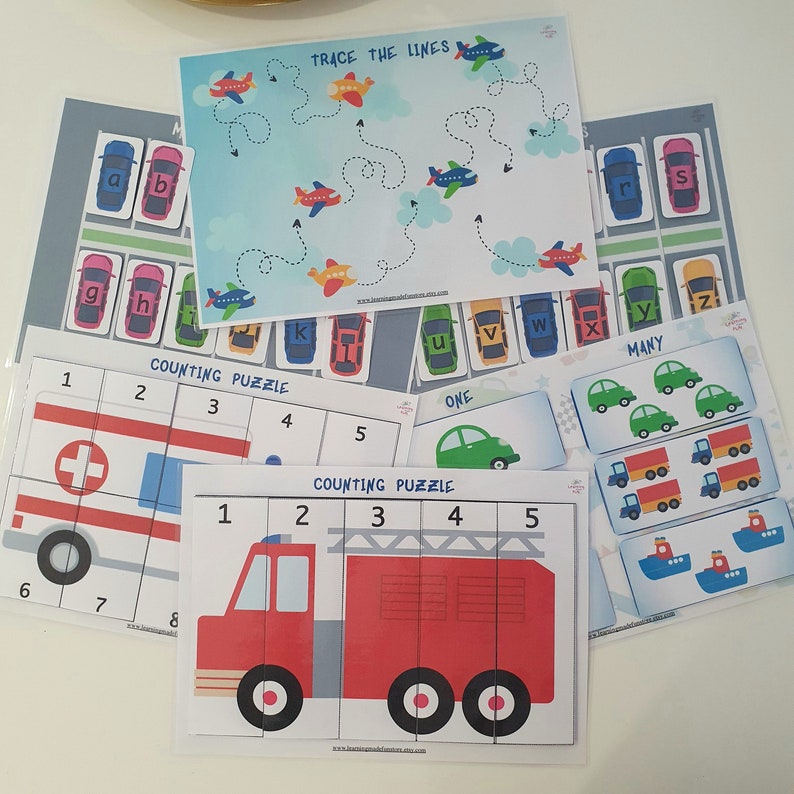 May include: A set of printable educational worksheets for kids featuring counting puzzles, tracing lines, and matching activities. The worksheets feature colorful illustrations of cars, ambulances, fire trucks, and airplanes. The text on the worksheets includes "Counting Puzzle", "Trace the Lines", "One", and "Many".