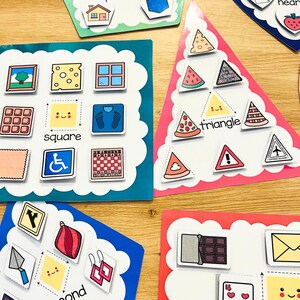 May include: A set of colorful educational flash cards with images and words for learning shapes. The cards feature a square, triangle, and other shapes with corresponding images.