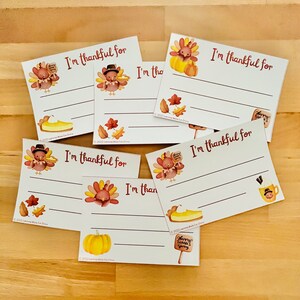 May include: Five printable Thanksgiving cards with an autumn theme. Each card features a different Thanksgiving-themed illustration, such as a turkey, pumpkin, pie, and autumn leaves. The cards have lines for writing "I'm thankful for..." and the text "Happy Thanksgiving!"