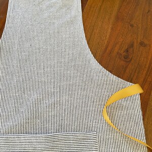 Peut inclure: Un tablier ray&eacute; noir et blanc avec un ruban jaune. Le tablier a une grande poche sur le devant.